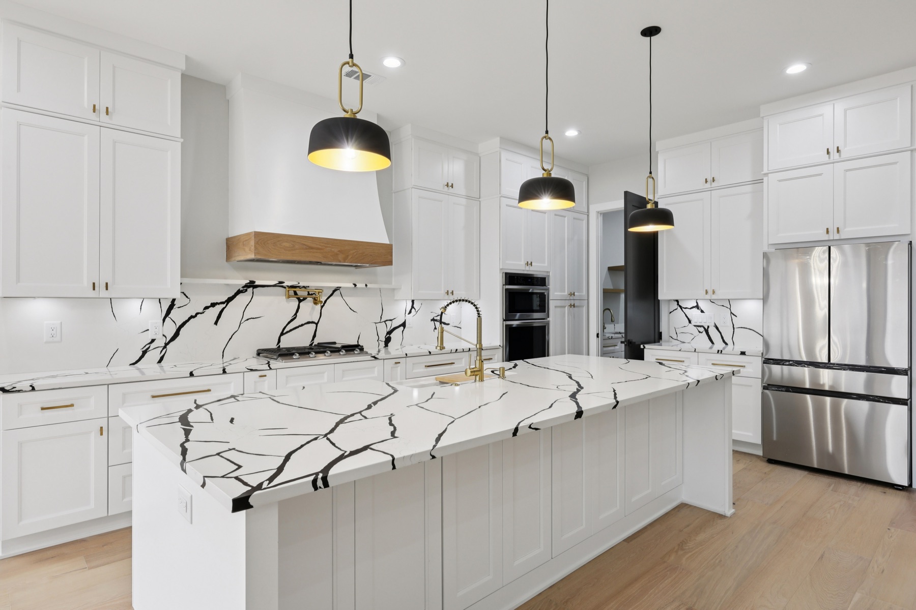 Chef's kitchen with a dramatic black-and-white marble waterfall island, custom wood-trimmed range hood, and gold fixtures