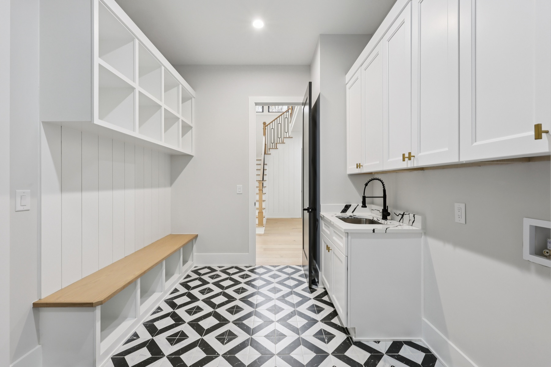 Mudroom and laundry with a built-in bench, open cubbies, and black-and-white patterned tile floor